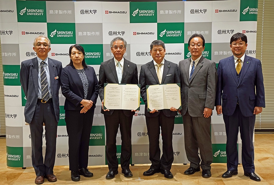 左から島津製作所分析計測事業部SolutionsCOEヘルスケアソリューションユニット副ユニット長 増田潤一、執行役員・分析計測事業部副事業部長 岡崎直美、代表取締役社長 山本靖則、国立大学法人信州大学長 中村宗一郎、理事（研究、産学官・社会連携担当）・副学長 向智里、アクア・リジェネレーション機構長　手嶋勝弥