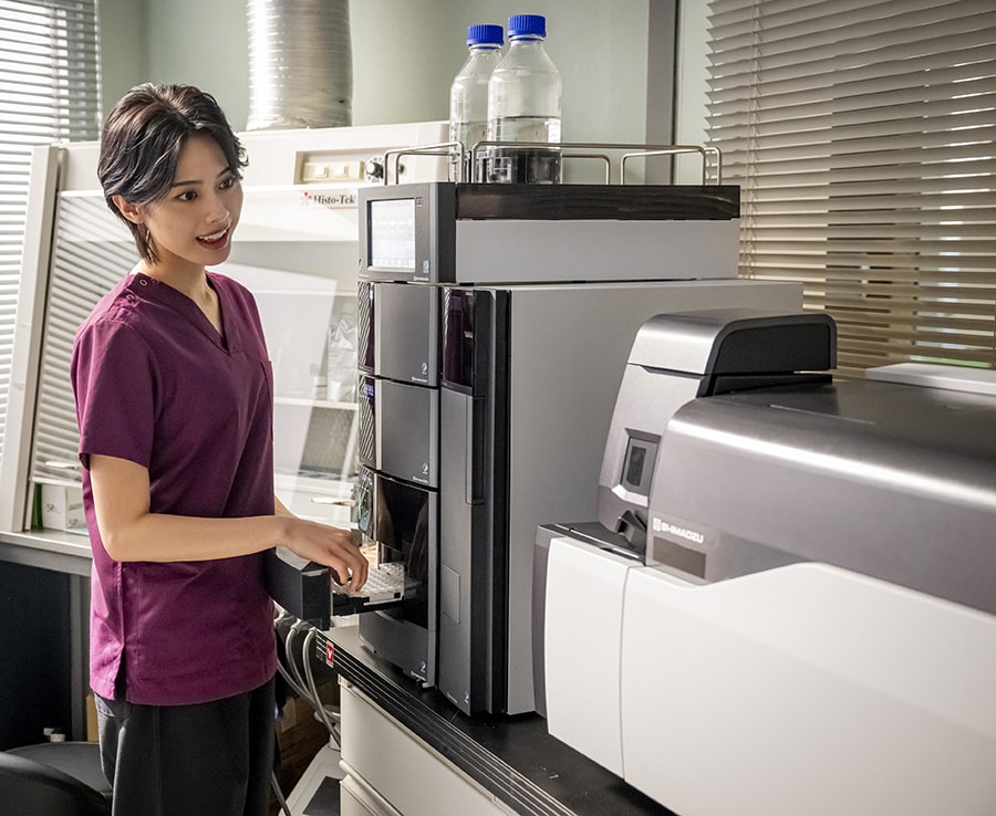 写真：高速液体クロマトグラフ質量分析計「LCMS-8050RX」と法医学者・松原涼音役の安斉星来さん