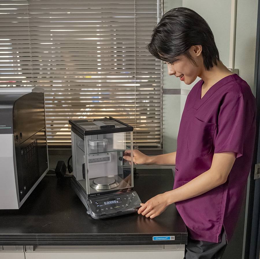 写真：分析天びん「AP225W-AD」と法医学者・松原涼音役の安斉星来さん