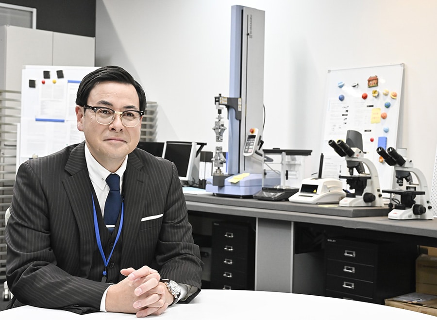 写真：東口亮治役の鈴木浩介さんと小型卓上試験機、分析天びん、水分計、生物顕微鏡2台