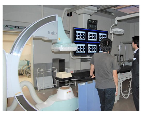 撮影スタッフに血管撮影システムの操作方法を説明する当社社員(右)