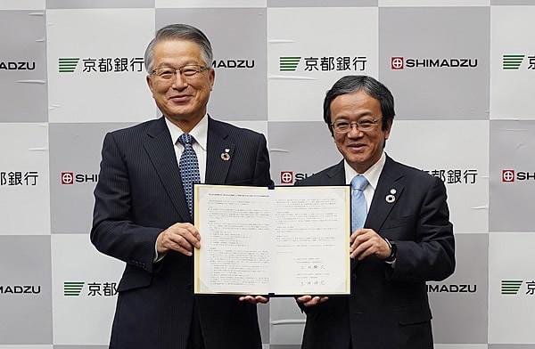 協定書を手にする土井伸宏・京都銀行取締役頭取（左）と上田輝久・当社会長(当時、社長)　（右）