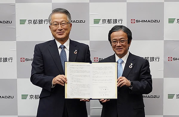 協定書を手にする土井伸宏・京都銀行取締役頭取(左)と上田輝久・当社会長(当時、社長) (右)