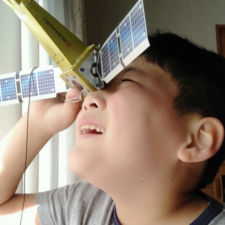 惑星分光観測衛星「ひさき」のペーパークラフトを覗く子ども
