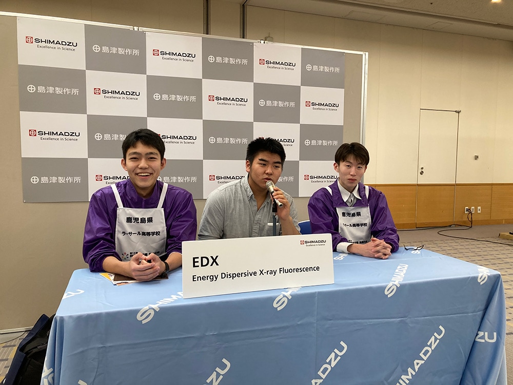 記者会見の会場を模したフォトスポットで、発表者になりきる選手たち