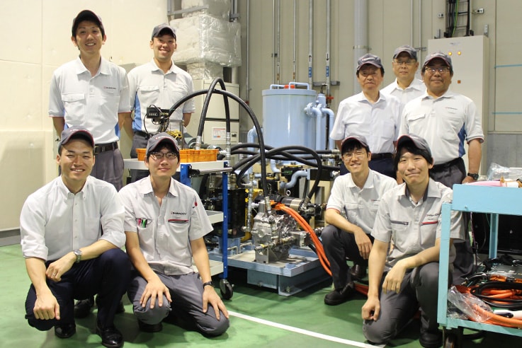 電動油圧システム「e-Hydro」（写真中央）と開発メンバー。上段左端が五島代介