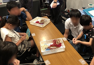 スタッフや保護者に見守られながらひもでロープを編む子どもたち