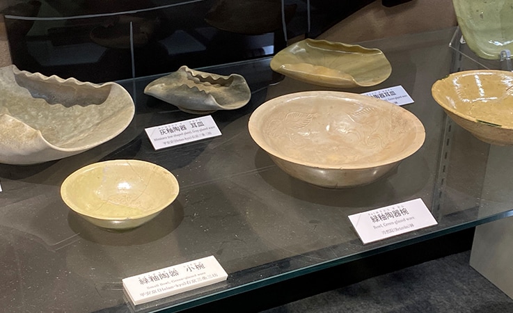 京都市考古資料館展示品　当社三条工場（三条三坊五町）から出土した緑釉陶器小椀（左手前）と、冷泉院から出土した緑釉陶器椀（中央手前）。いずれも光を反射するような艶が特徴的　