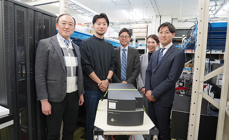 左から理化学研究所の南出泰亜さん、瀧田佑馬さん、島津製作所の平岡亮二、坂本怜美、西亮祐。 中央には光スペクトラムアナライザ「SPG-V500」。