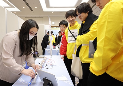 企業出展コーナーで実験キット 力学台車「コイルを通過する磁石トレイン」 を演示する島津理化の社員 