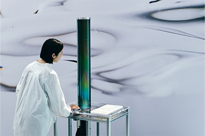 「Optical Rotation」砂糖が持つ光をねじる性質を用いた作品。砂糖水で満たした筒を下から照らす光は、色（波長）ごとに異なる角度にねじれる。つまみを回すと一部の光だけ通す偏光板が動き、色の見え方が変化する
