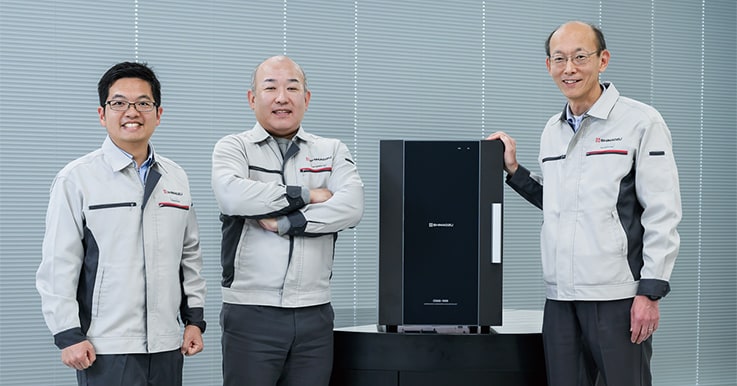 複合劣化促進ユニット「CDAS-1000」と分析計測事業部技術部の開発メンバー。(右から)アナライザーG グループ長 小田竜太郎、新事業開発推進G 主任 長谷川雪憲と主任 加藤裕樹